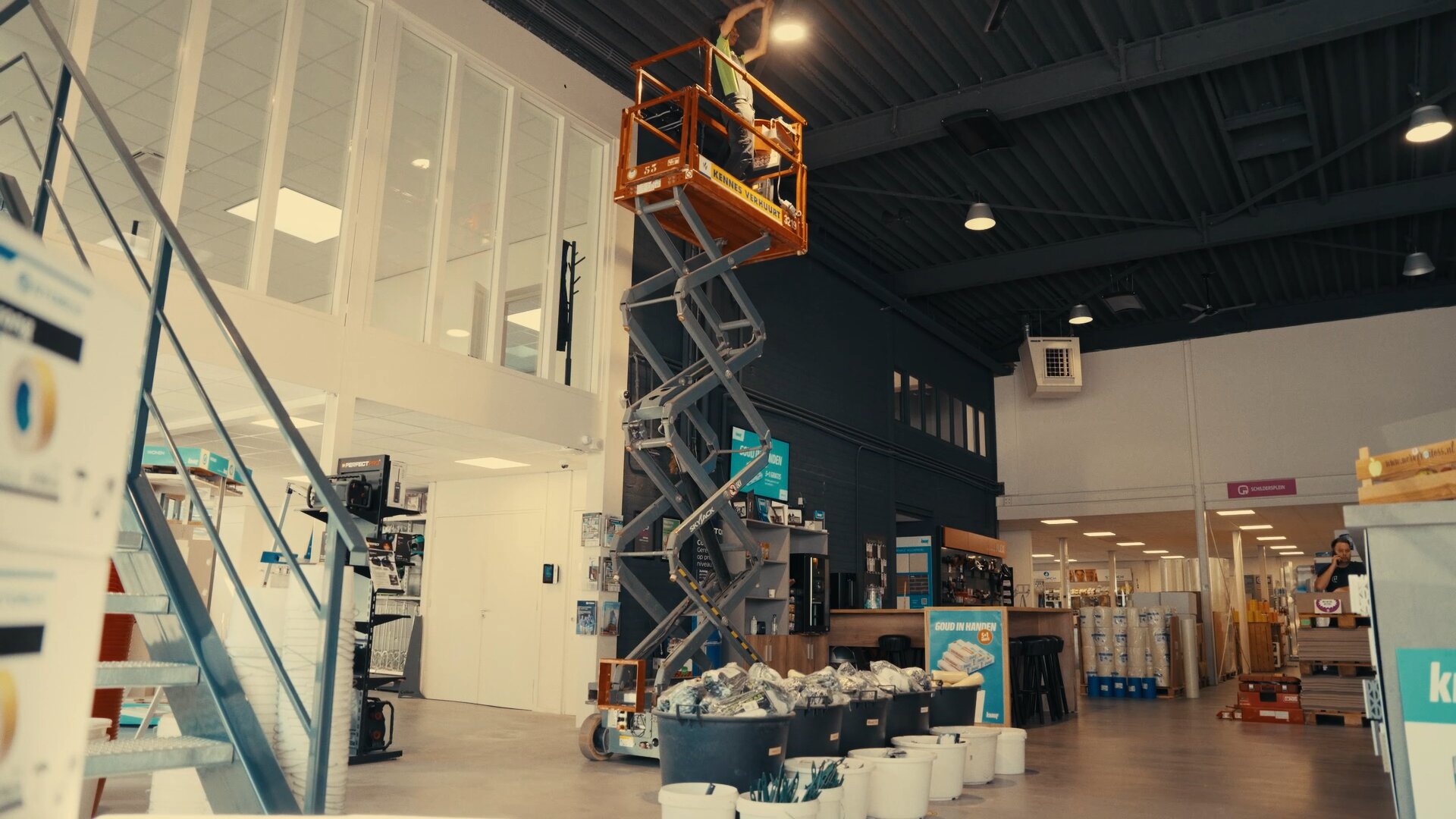 Monteur op een schaarhoogwerker werkt aan de plafondverlichting van een winkel die open is.
