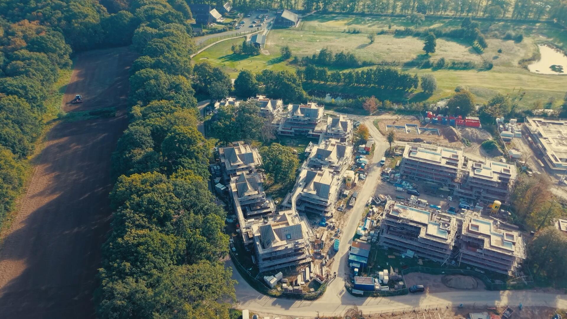 Nieuwbouwwoningen in aanbouw met steigers, van bovenaf gezien tussen bos en weilanden.