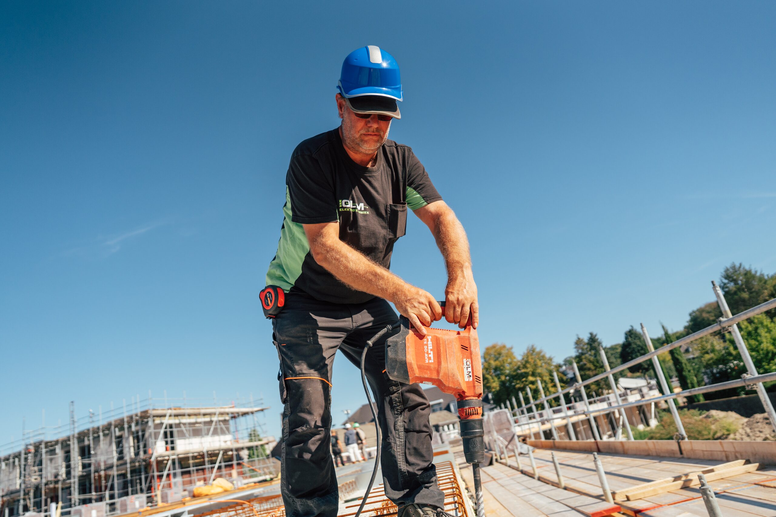 Monteur met blauwe helm boort met een Hilti-boorhamer in een betonvloer in aanbouw.