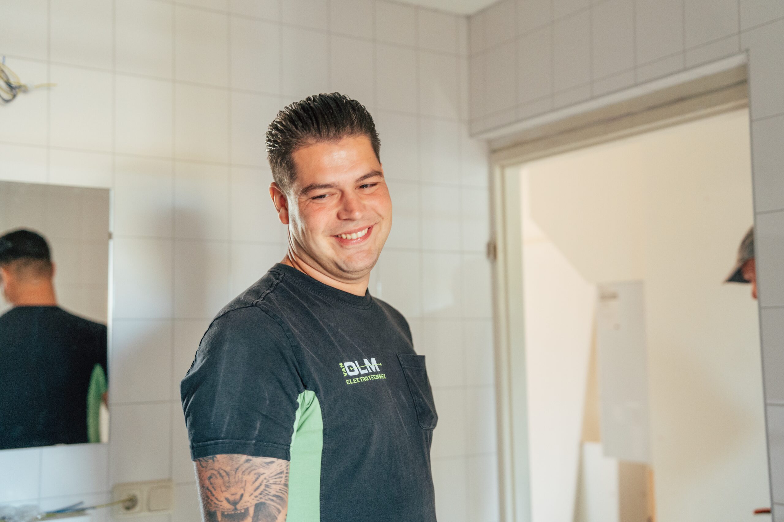 Lachende monteur van Van Olm Elektrotechniek in een betegelde badkamer die wordt verbouwd.