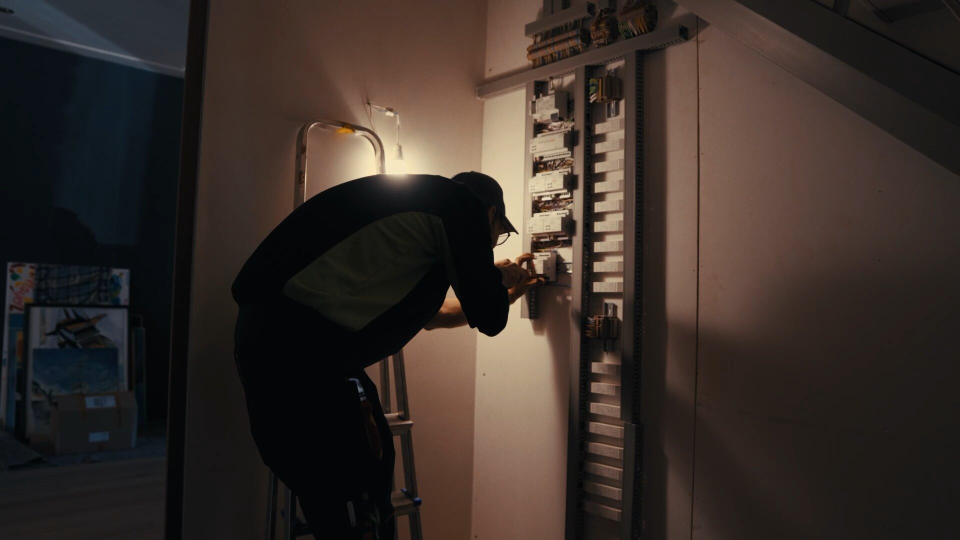 Monteur werkt bij lamplicht aan een open verdeelkast onder de trap van een woning.